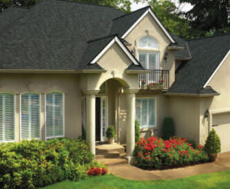 GAF Designer Grand Sequoia example roof in charcoal on a stucco house with a balcony and flower beds.