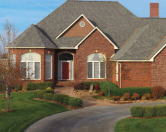 GAF Designer Grand Sequoia in Weathered Wood roof shingles. Brick house with lawn and driveway.