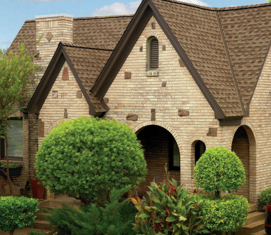 GAF Timberline ArmorShield II example roof in Shakewood color. Brick house with Shakewood ArmorShield II roofing shingles, arched doorways, and manicured landscaping.