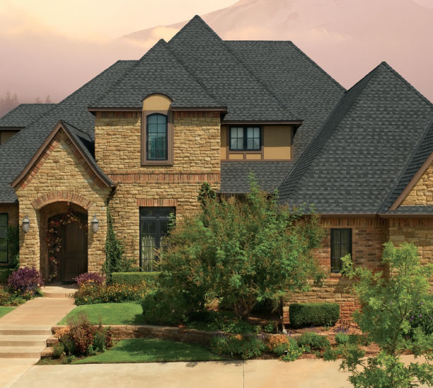 GAF Timberline HDZ in Charcoal on a stone house. Example roof with architectural style and mountain backdrop. Durable roofing shingles.