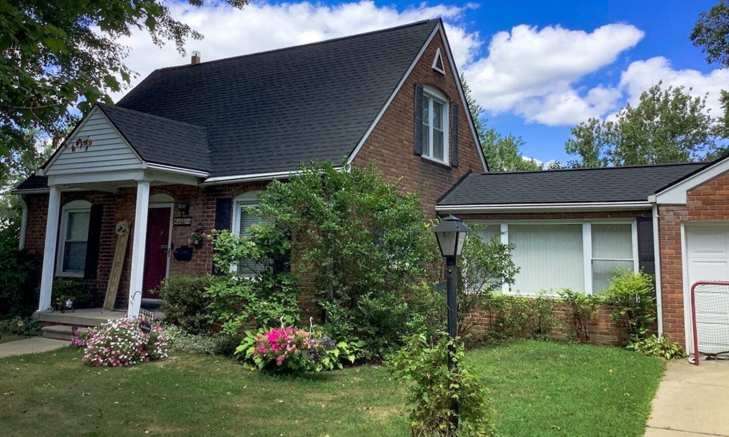 Garden City roof replacement. Front view of a brick house with a new roof. Trees surround the home. Roof Advisor services.