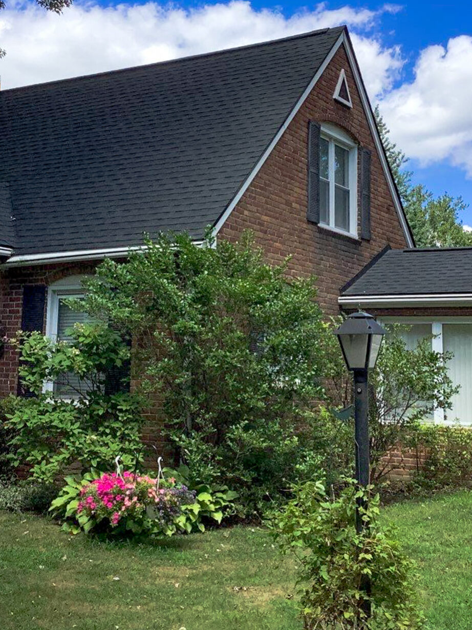 Garden City roof replacement. Front view of a brick house with a new roof. Trees surround the home. Roof Advisor services.