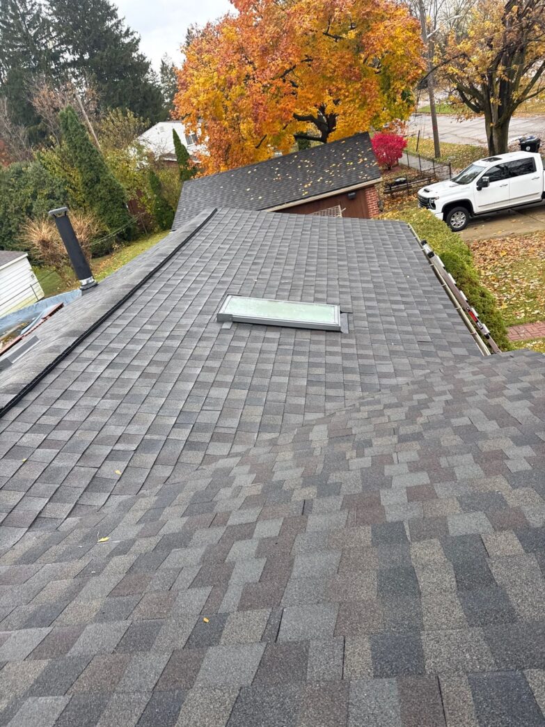 Leila A's 5-Star Roofing in Redford: A view of the completed roofing project, showcasing the new shingles and a skylight, with autumn foliage visible.