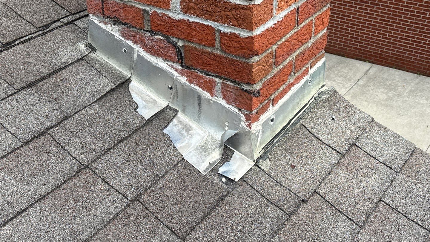 Leila A's Redford home before 5-Star Roofing repair: Damaged chimney flashing on shingled roof. Professional roofing services needed in Redford.