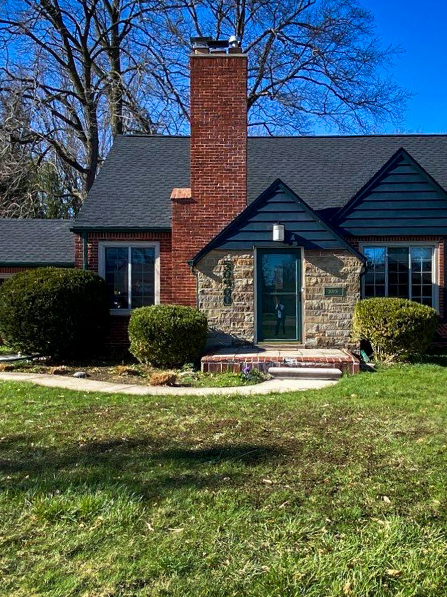 Livonia Rayburn roof replacement. Front view of a brick house with a new roof. Landscaped lawn and blue sky on a sunny day.