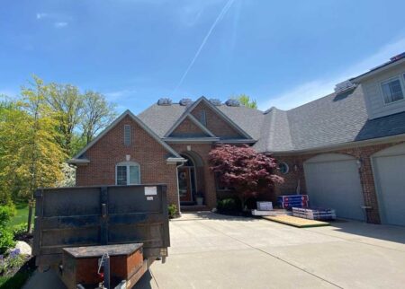 Material delivery for a New Baltimore roof replacement project. Shingles on the roof, dumpster in front of a brick house ready for debris removal.