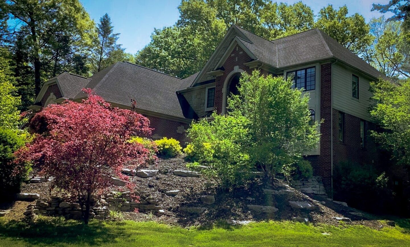 Milford Hill Hollow roof replacement. A house with a unique roof design is surrounded by trees. The front of the home is visible.
