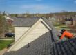 Multi-family roof maintenance. Roofer repairing a gray asphalt shingle roof on a house in a suburban neighborhood. Professional roofers at work.