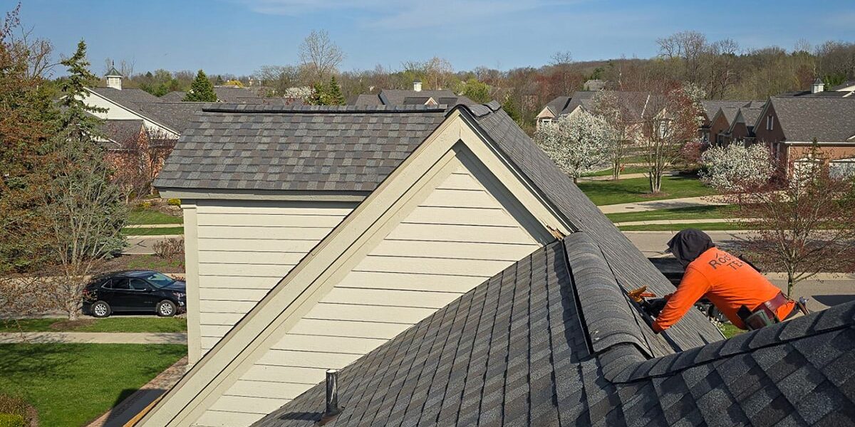 Multi-family roof maintenance. Roofer repairing a gray asphalt shingle roof on a house in a suburban neighborhood. Professional roofers at work. Multi-family roof maintenance. Roofer repairing a gray asphalt shingle roof on a house in a suburban neighborhood. Professional roofers at work.