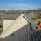Multi-family roof maintenance. Roofer repairing a gray asphalt shingle roof on a house in a suburban neighborhood. Professional roofers at work.