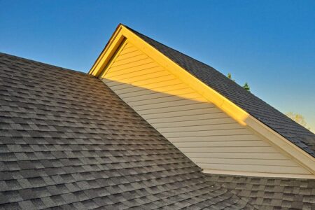 Newly replaced multi-family roof. Asphalt shingles on a building with light siding against a blue sky. Roofing bids for multi-family homes.