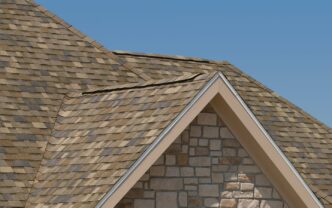 Owens Corning Duration Designer Ridge Shingles in Sand Dune on a home. The architectural shingles complement the tan stone exterior and blue sky. Roofing shingles.