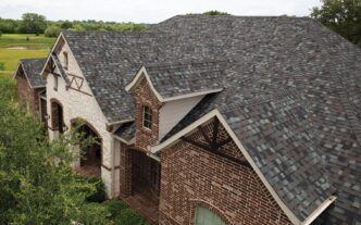 Owens Corning Duration Designer Shingles in Storm Cloud color on a home. The roof features a blend of gray and brown hues, complementing the brick and stone facade.