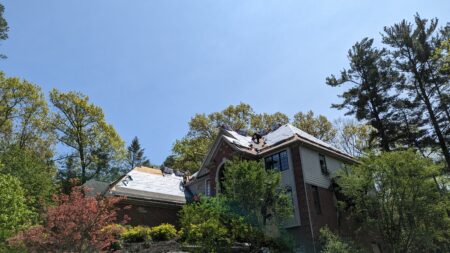 Professional Job done in one day: Milford roof installation testimonial: Workers installing a new roof on a large house surrounded by trees under a blue sky. We get the job done.