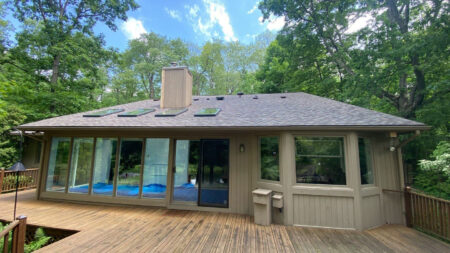 Pool house Canton roof replacement after by Bruce's. Features new gray roof, skylights, chimney, and wooden deck surrounded by trees. Canton, OH.