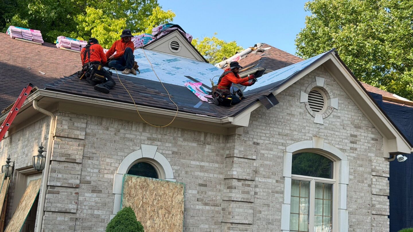 Roofers install new shingles and underlayment on a large house roof during the roof replacement project