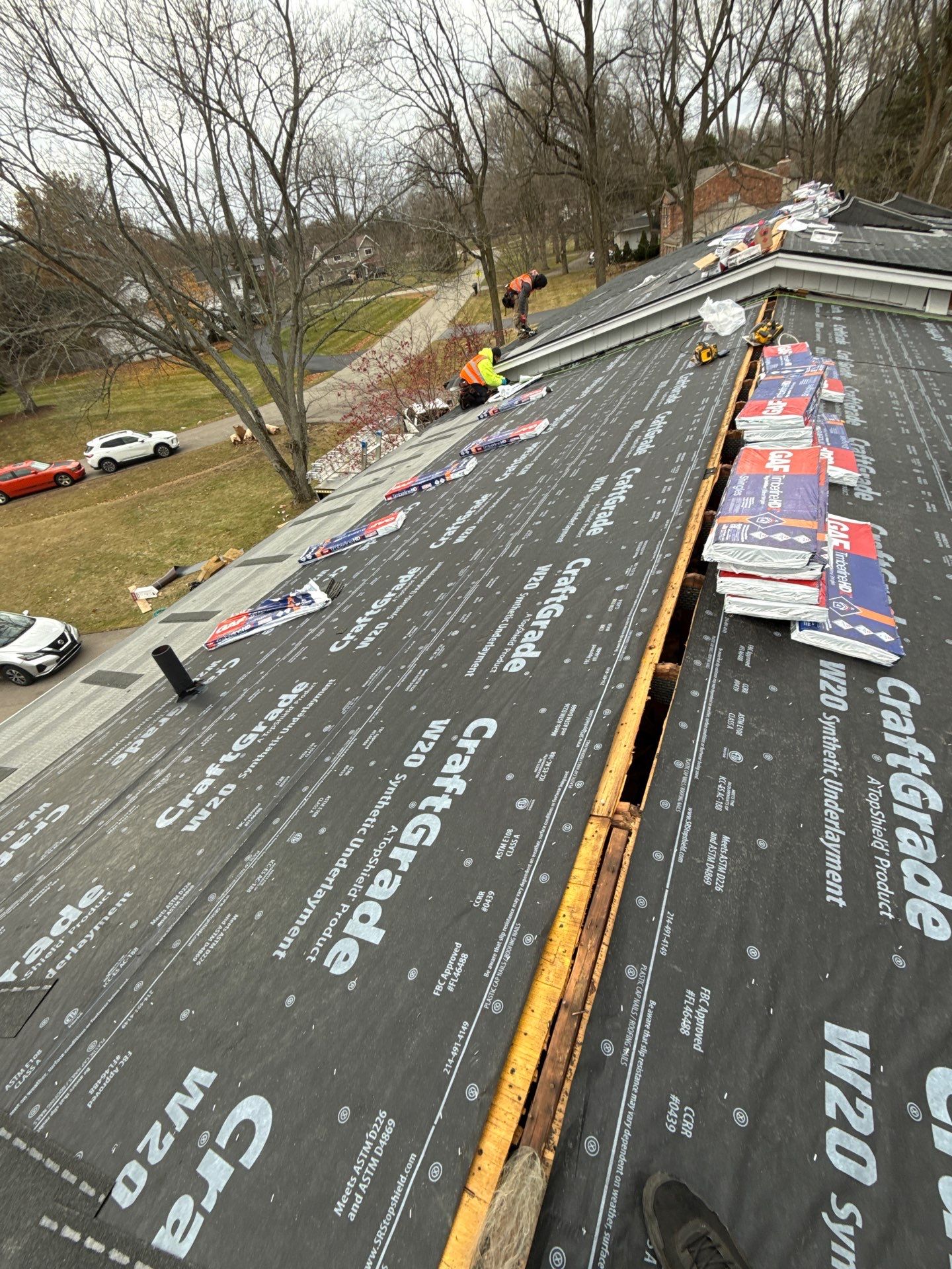 A residential roof under construction with black waterproof underlayment installed and roofing materials stacked nearby.