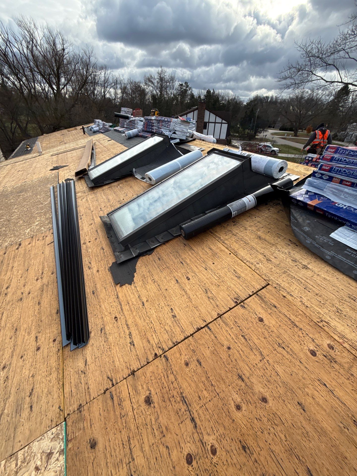 Partially completed roof with exposed wooden decking, skylights installed, and cloudy sky in the background.