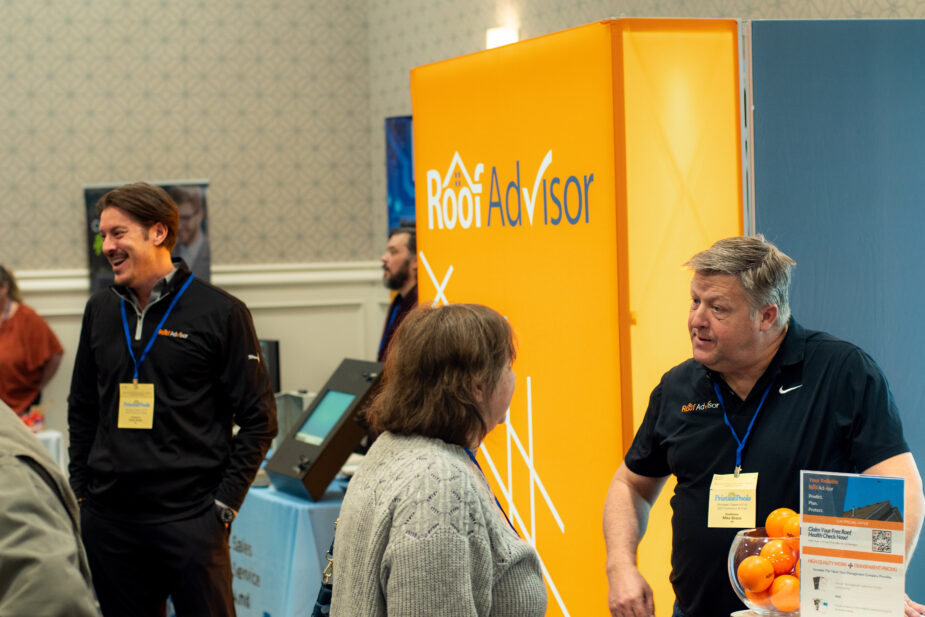 RA CAI Expo booth featuring Roof Advisor representatives in conversation, showcasing brand display and informational materials. Promoting roof assessment services.