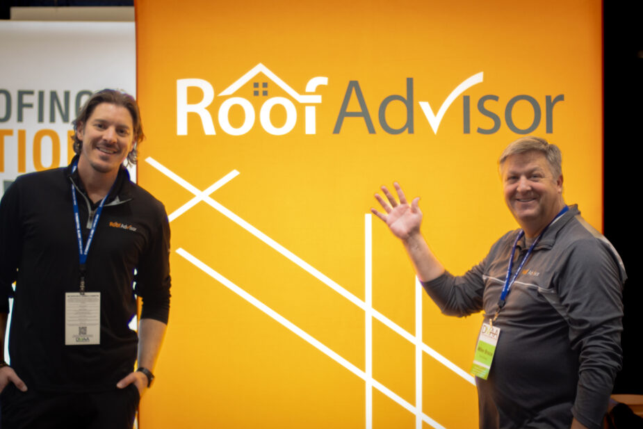 Roof Advisor DMAA Expo: Two men pose in front of a branded backdrop. One waves, showcasing the roofing advisor company at the expo event. 