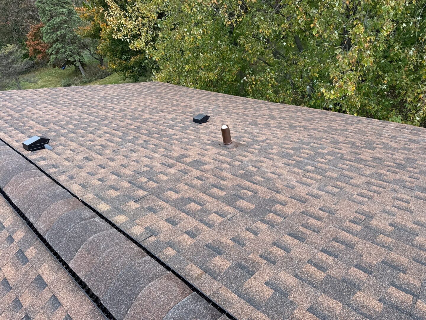Completed residential roof replacement in Livonia featuring textured brown architectural shingles, two black ventilation hoods, and a central pipe vent.