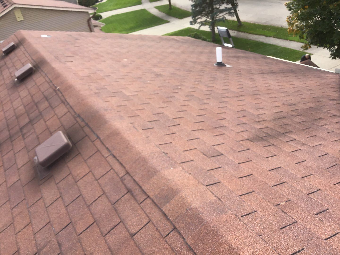 Weathered brown asphalt shingles on an existing residential roof in Livonia featuring three square attic vents and a single white plumbing pipe fixture.
