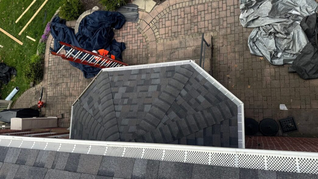 Roofing work in progress with tarps, ladders, and shingles on a house roof and patio below