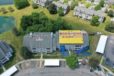 Great service for multi-family roof replacement testimonial: Aerial view of apartment complex with half of the roof replaced, showcasing roofing project progress. Quality work clearing away all storm damage.