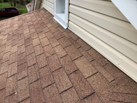 Before Westland roof replacement showing the wall intersection with old brown shingles and beige siding needing repair or replacement, shot at an angle.